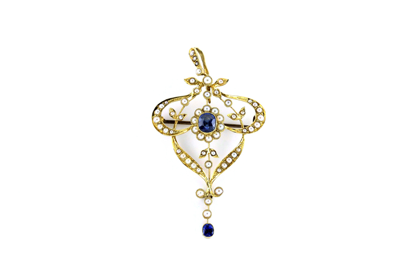 An Edwardian 15ct gold shield shaped pendant, set with numerous seed pearls and a sapphire centre