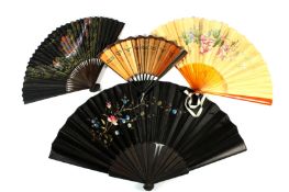 A small collection of four fans comprising a black embroidered fan with wooden sticks, one with