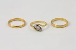 An 18ct gold three stone diamond ring in swirl shape setting, together with two 22ct gold wedding