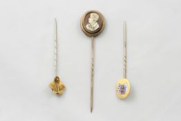 Three gold stick pins comprising a cameo of a young boy, one decorated with three enamelled cards,