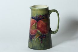 A Moorcroft pottery `Pomegranate` tall jug circa 1920, of tapered form on mottled green ground, with