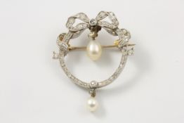 An Edwardian circular pearl and diamond brooch with bow decoration to top set with numerous small