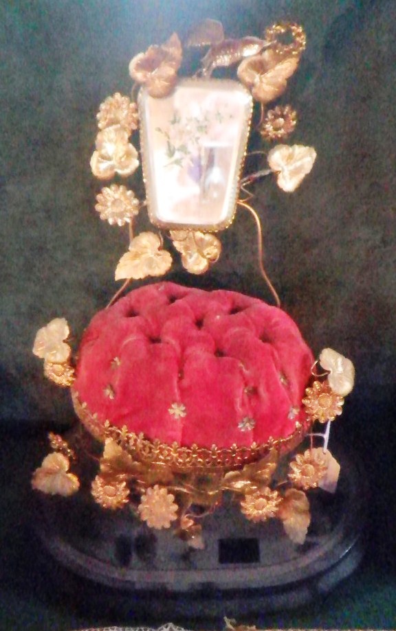 An Edwardian hat pin display stand, fashioned as a red plush covered cushion, contained within a