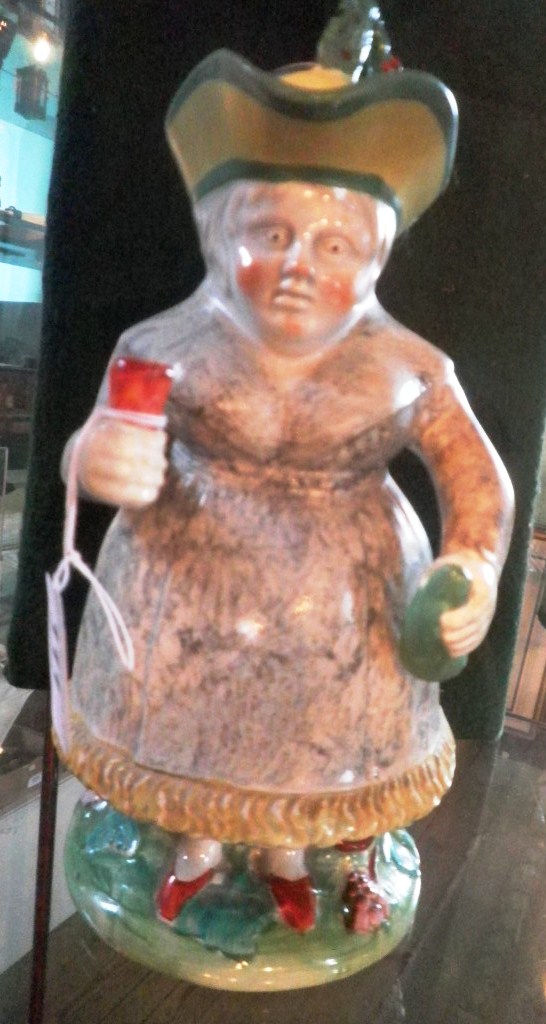 A mid-19th century toby jug fashioned as the Gin Woman with tricorn hat, holding a bottle and