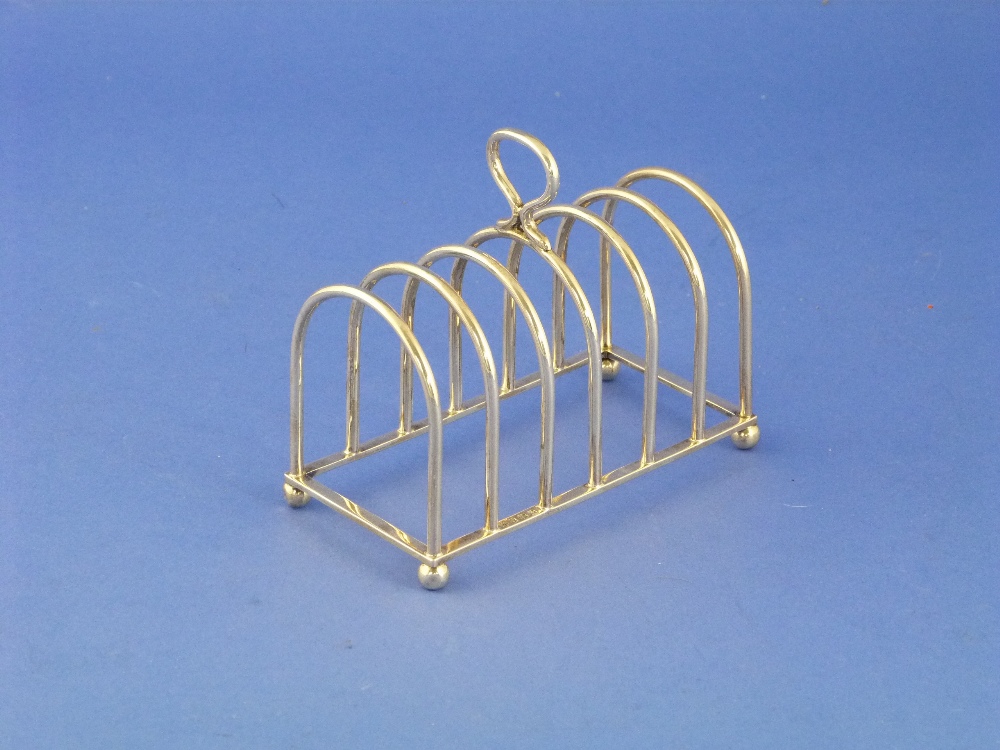 A George V silver Toast Rack, hallmarked Birmingham, 1928, with seven arched bars, on ball feet, 5in