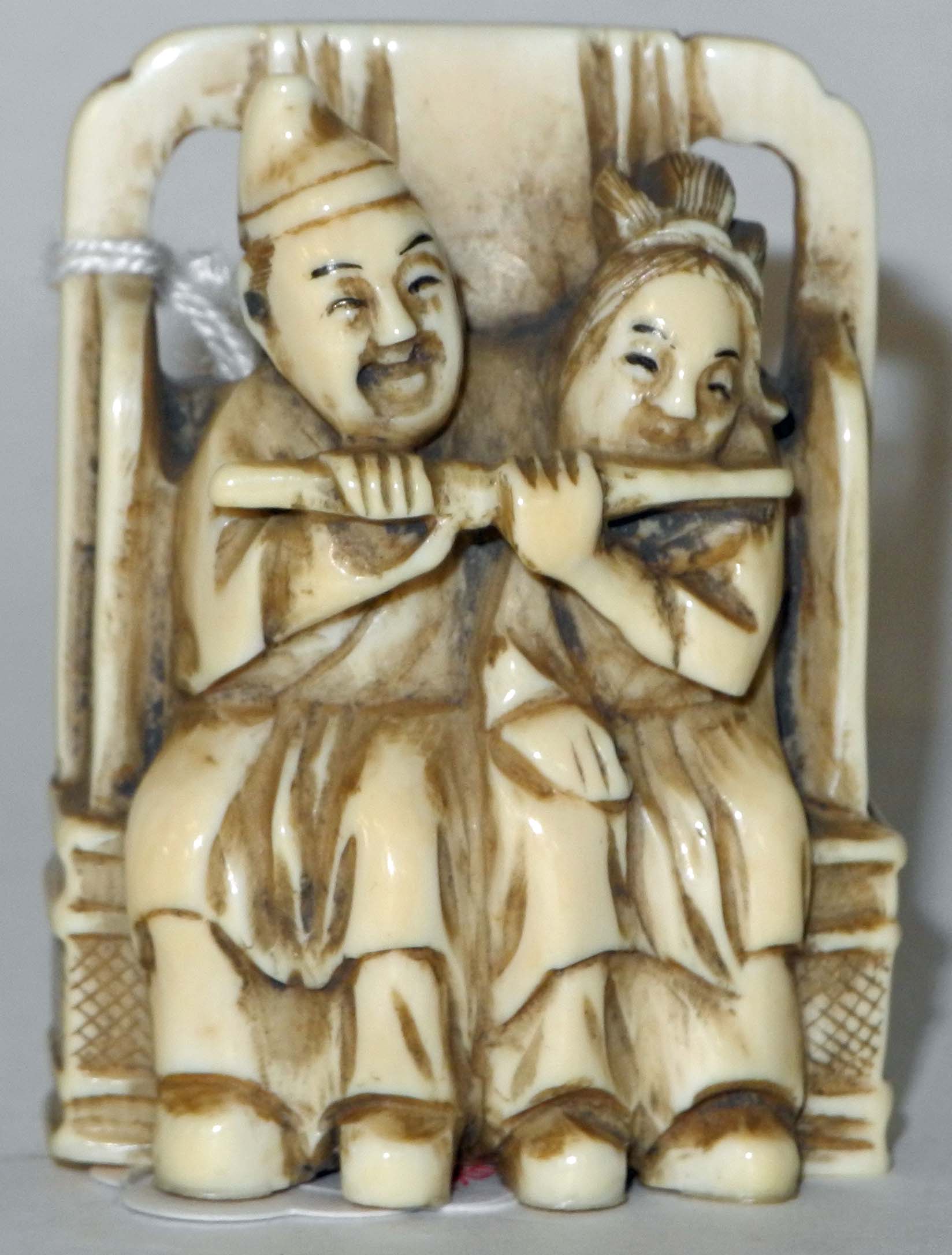 A Japanese ivory netsuke of two figures seated on a bench playing a pipe, signed.5cm