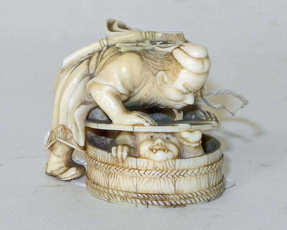 A Japanese ivory netsuke of a male figure pushing a beast into a wooden barrel, signed.3cm