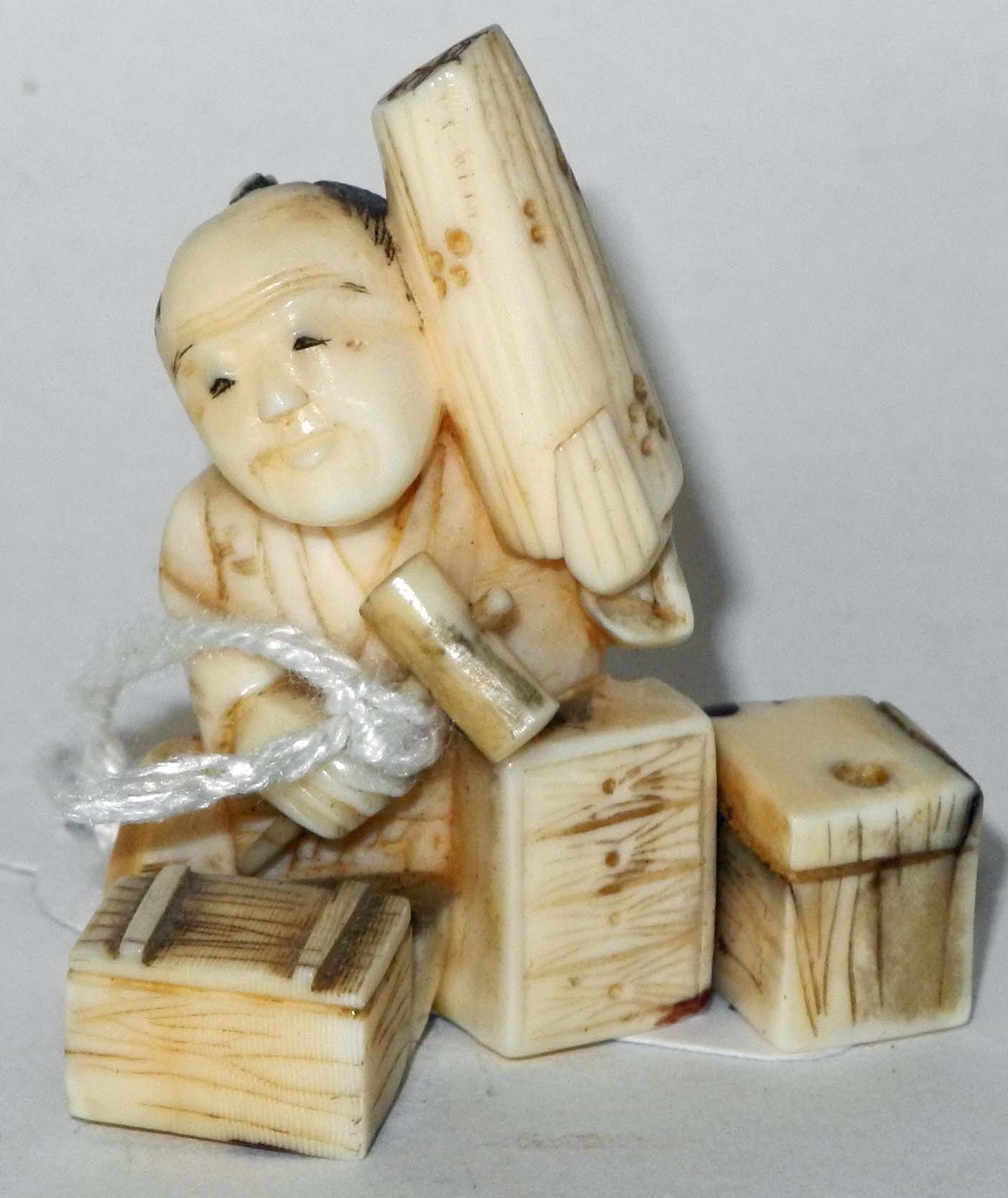 An antique ivory netsuke of a carpenter with boxes and a mallet.4cm