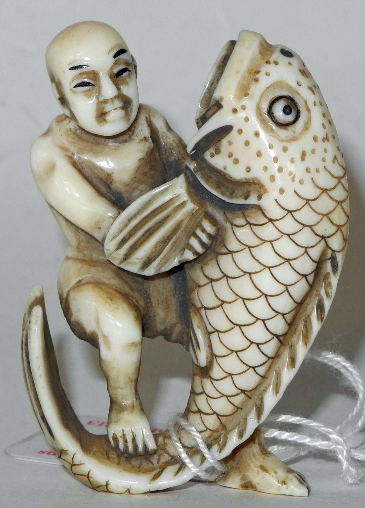 A Japanese ivory netsuke of Ebisu grappling with a huge fish, signed.5.5cm