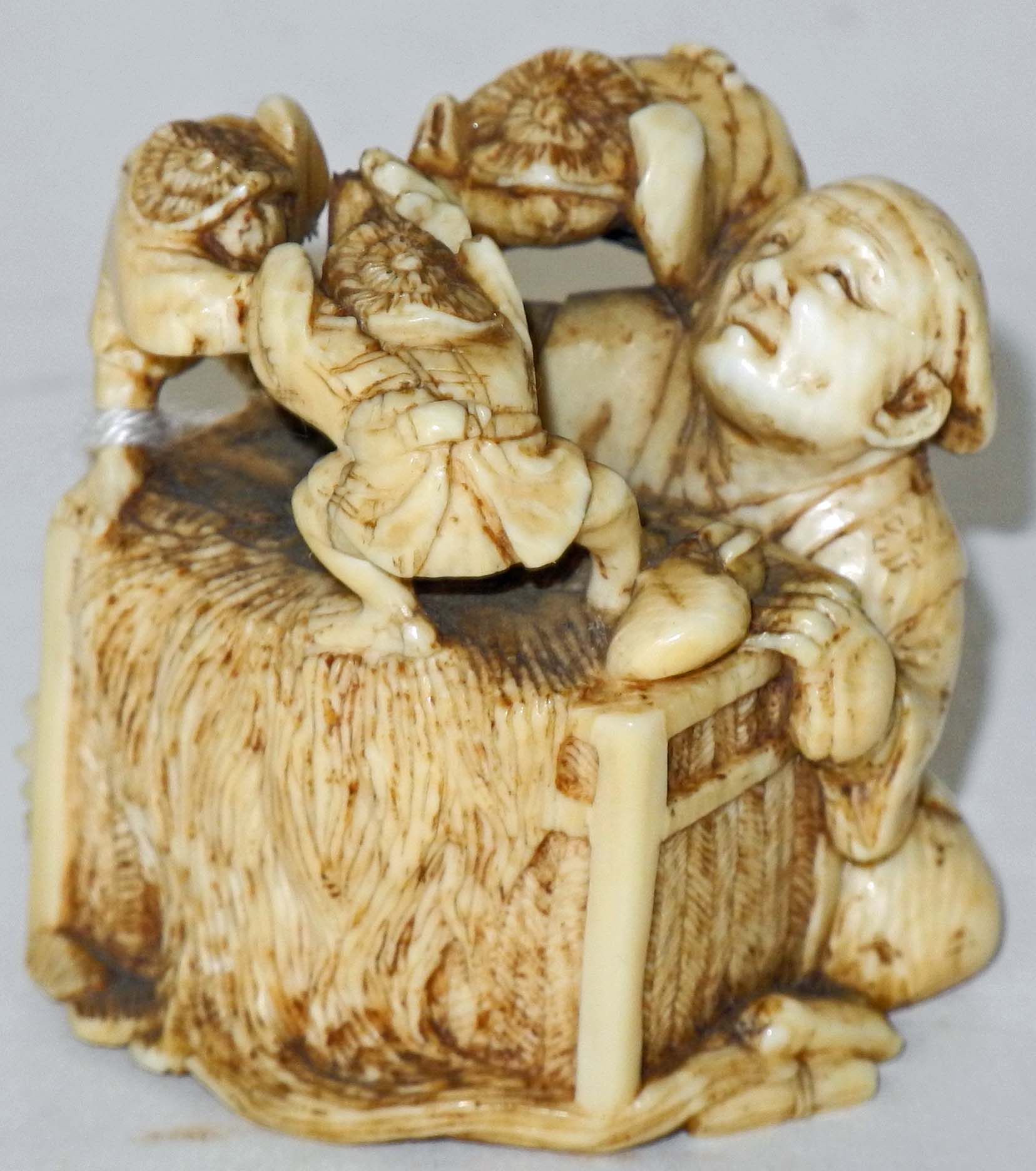 A Japanese ivory netsuke of a seated man by a box and three fighting dwarf figures.4cm