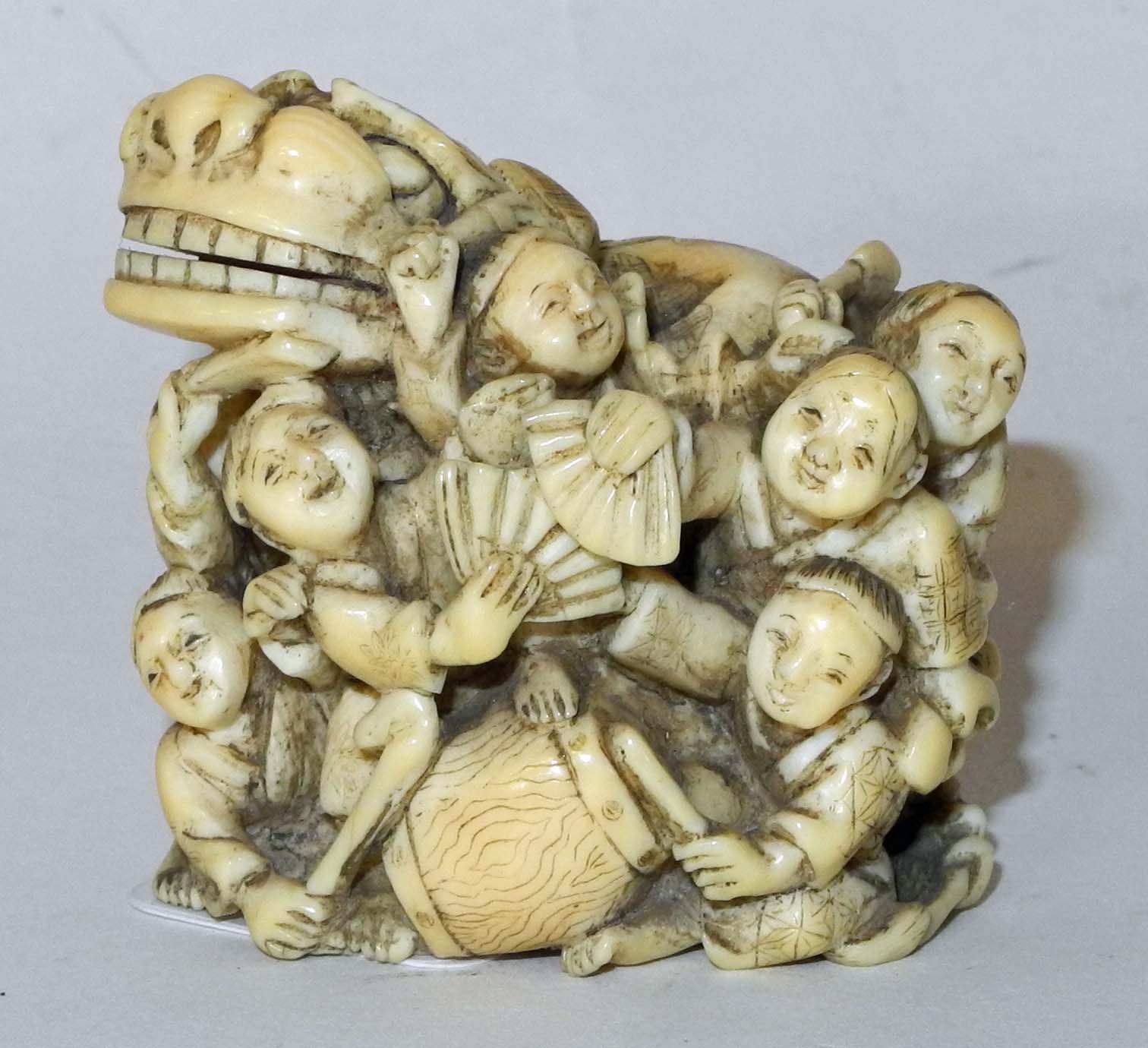 A large Japanese ivory netsuke of a group of children playing with a lion dog, signed in red lacquer