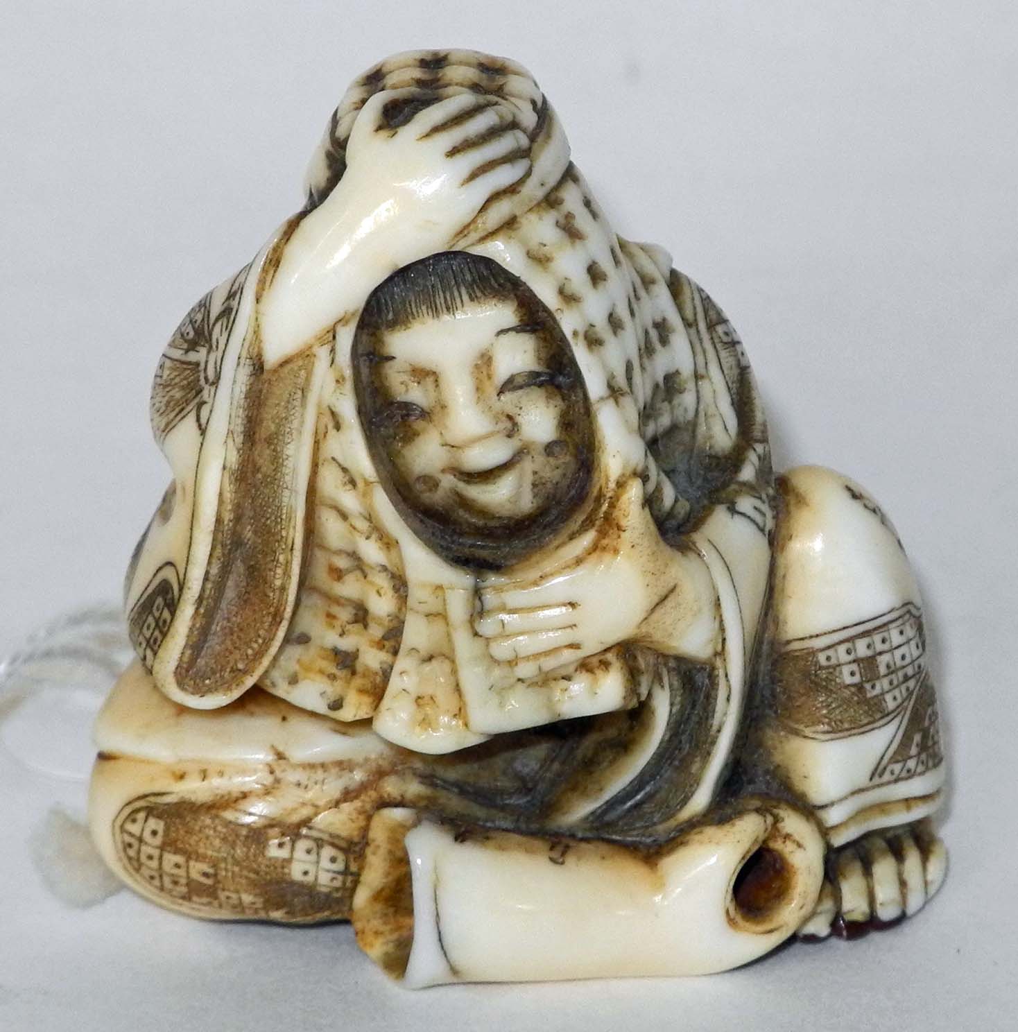 An antique ivory netsuke of a man hiding under a blanket, with a glove at his feet, signed.3.5cm