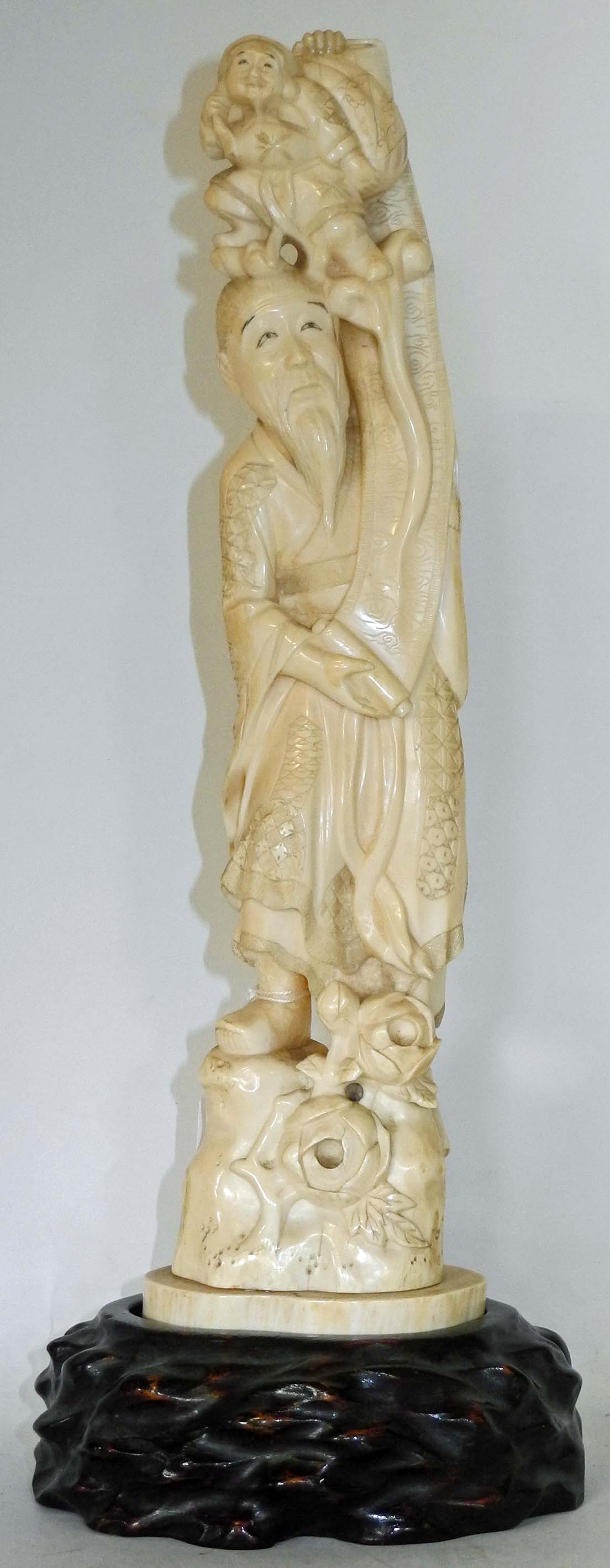 A large antique Japanese ivory carving of a sage standing with a child on his head, on wooden