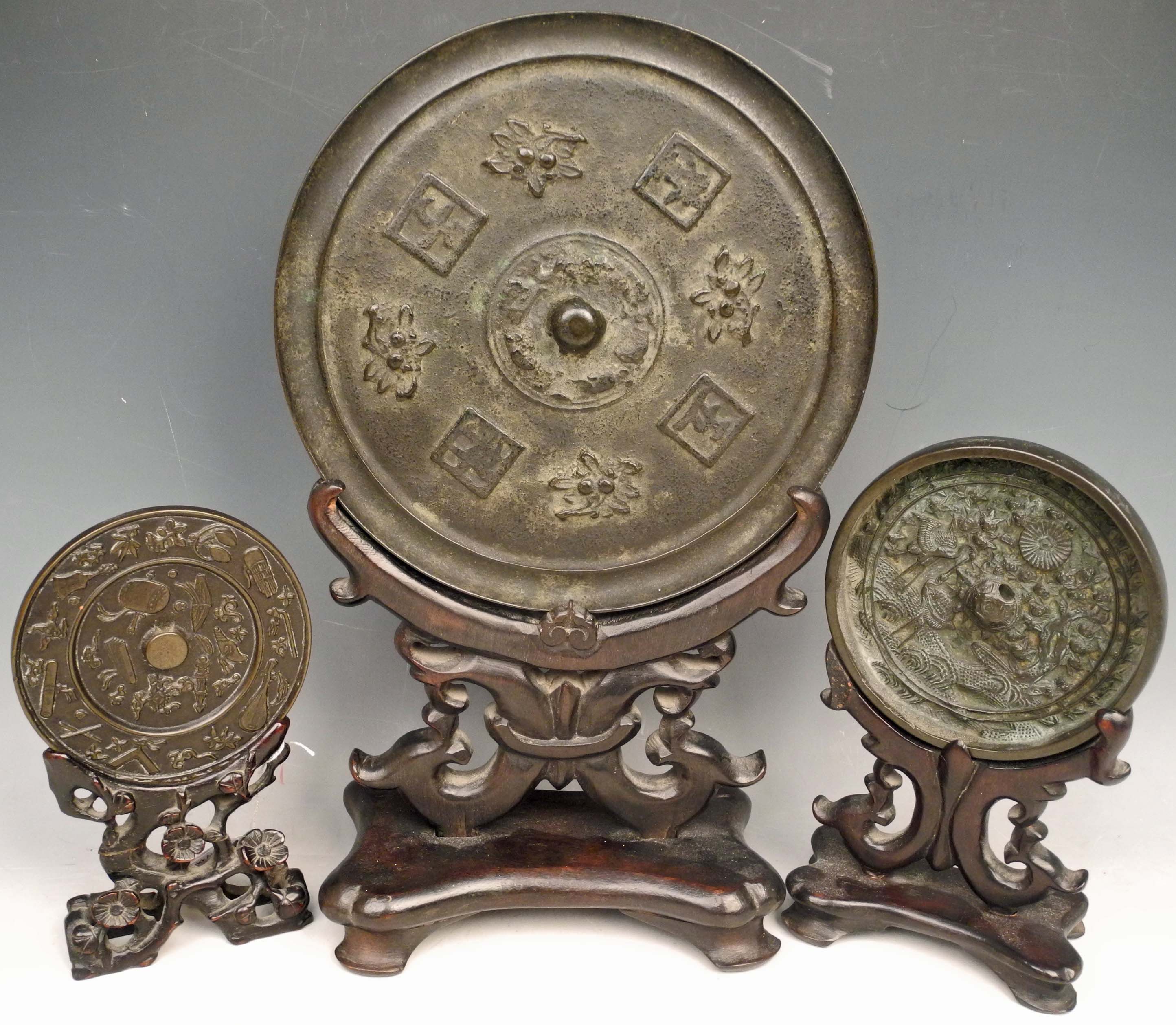 An antique Chinese bronze pi mirror on wooden stand, together with two others smaller. (3)