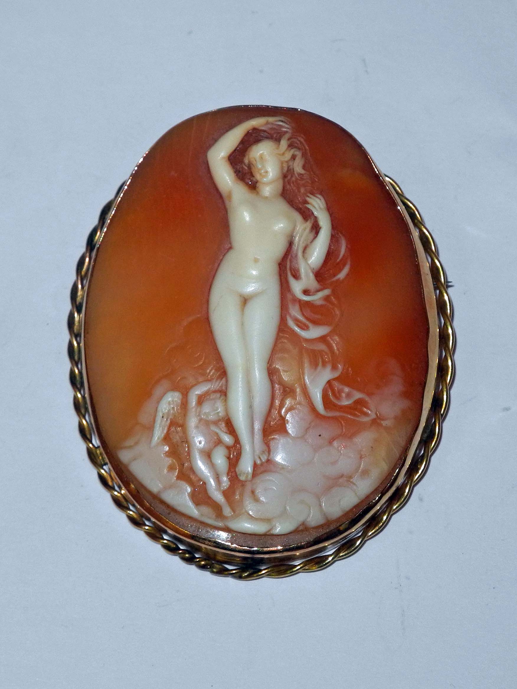 A late 19th Century cameo brooch, a standing nude with winged putti to her feet, in yellow metal