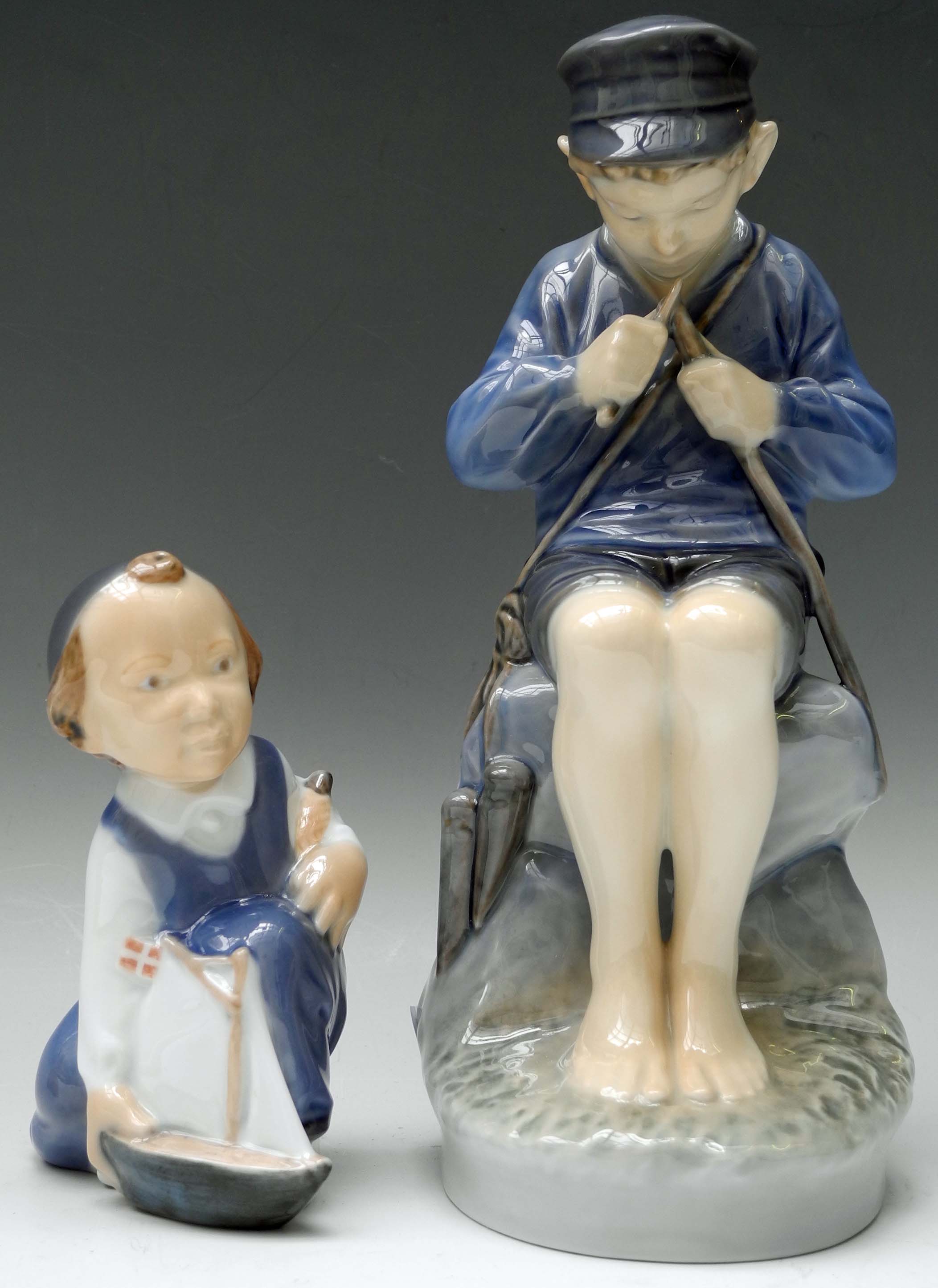 A Royal Copenhagen figure of a seated boy whittling a stick, together with another figure of a child