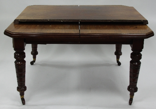 A late Victorian mahogany dining table, the canted rectangular top on turned legs with castors,