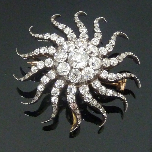 A diamond sunburst brooch/pendant centred by a cluster of nine diamonds radiating fourteen diamond