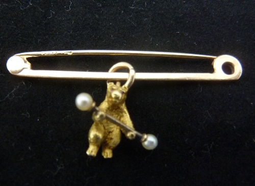 A gold bar brooch hung with a model of a bear holding a dumb-bell, the bear with gem set eyes, the