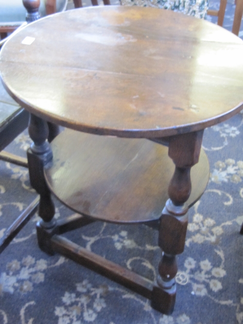 A circular oak two tier country table resting on three turned and cross stretcher supports.