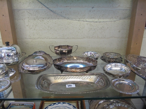 A shelf containing a quantity of silver plated items together with a box of green felt silver bags.