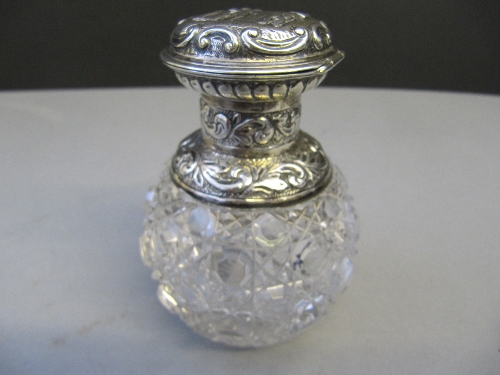 A late 19th century cut glass scent bottle with decorative silver lift-top lid decorated with
