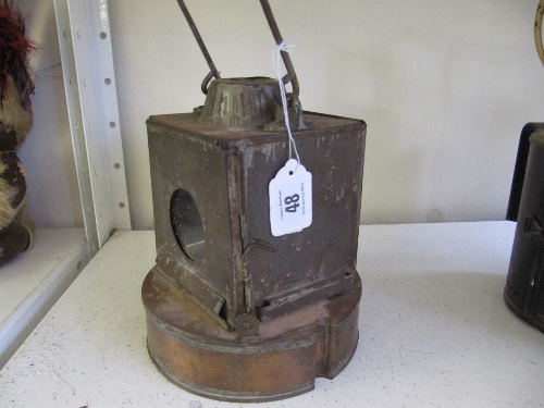 A square Copper Lamp with clear lens to the front and rear on a circular tank with burner.