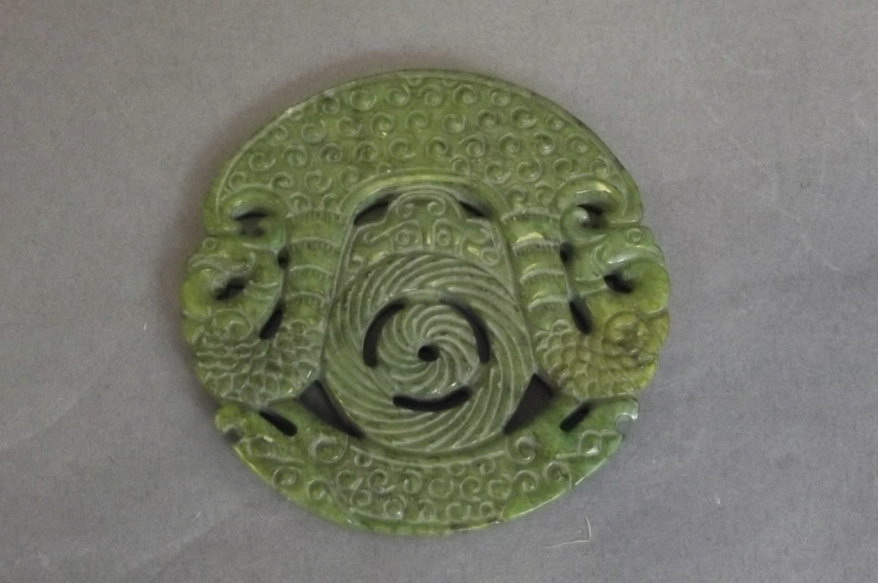 A Chinese pierced mottled green hardstone circular pendant with carved phoenix and dragon