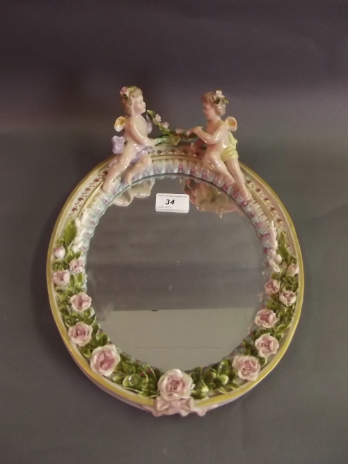 A continental porcelain framed wall mirror decorated with cherubs and garlands of flowers, 13'' x
