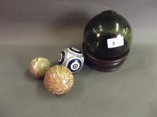 A coloured glass ball in a mahogany coaster, 5'' diameter, and 3 early C20th composite balls