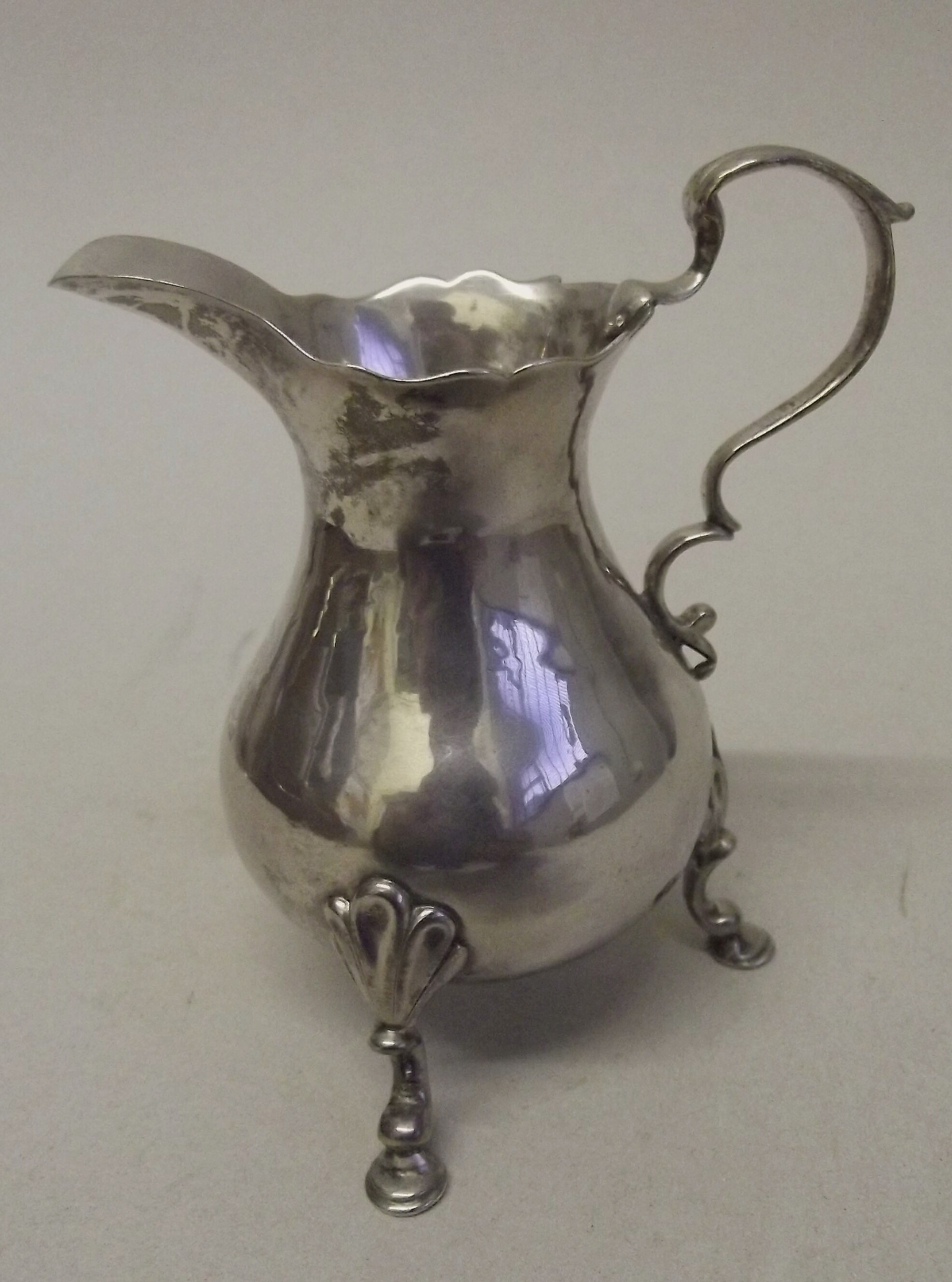 A George II cream jug with 'c' scroll handle on three shell capped, 'c' scroll legs with pad feet,