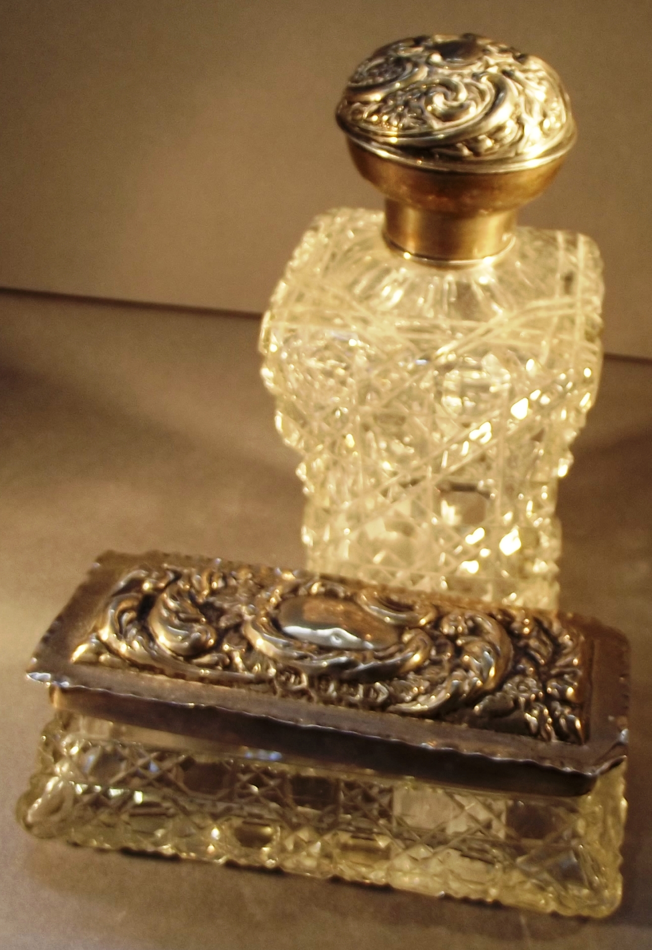 An Edwardian weighted square section cut glass toilet bottle with embossed silver lid, together with