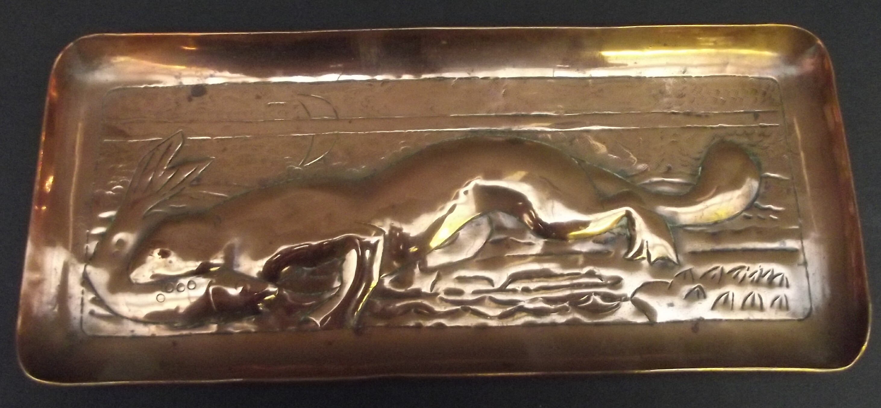 A Newlyn copper pen tray embossed with a sea otter with a fish in its mouth, width 20cm.