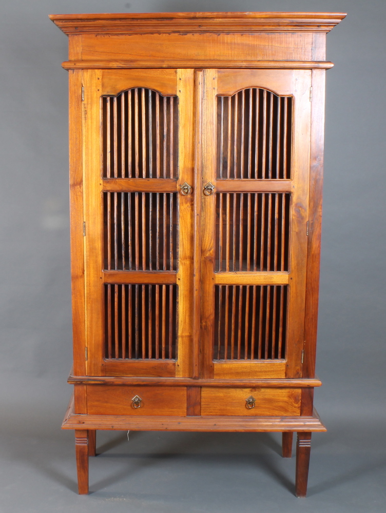 A hardwood cabinet enclosed by lattice panelled doors above 2 drawers with brass drop handles,