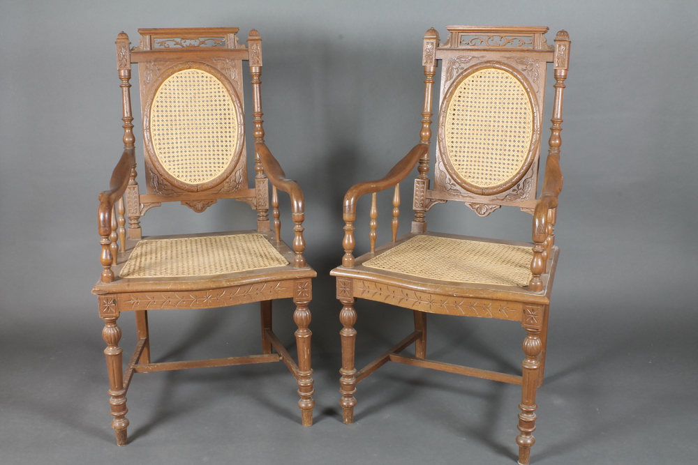 A pair of Eastern carved hardwood open arm chairs with  upholstered seats and backs raised on turned