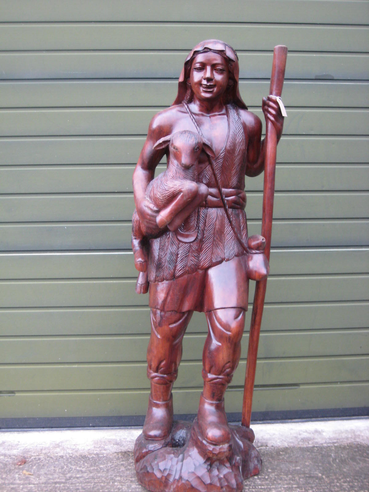 A large carved wooden figure of a shepherd carrying a pet lamb, and a staff 158 cms high