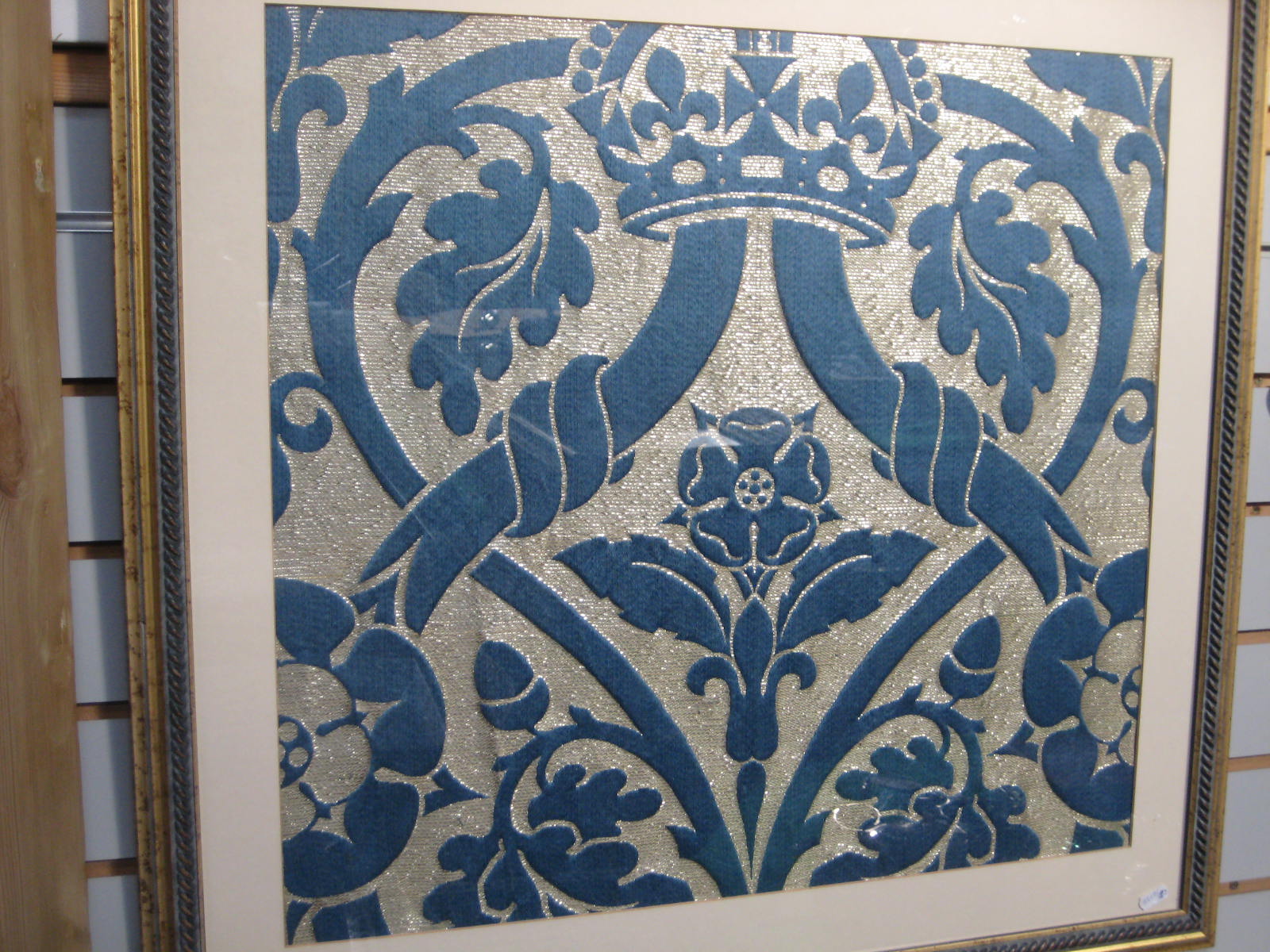 A silver thread and blue embroidered panel of a crown above a floral display