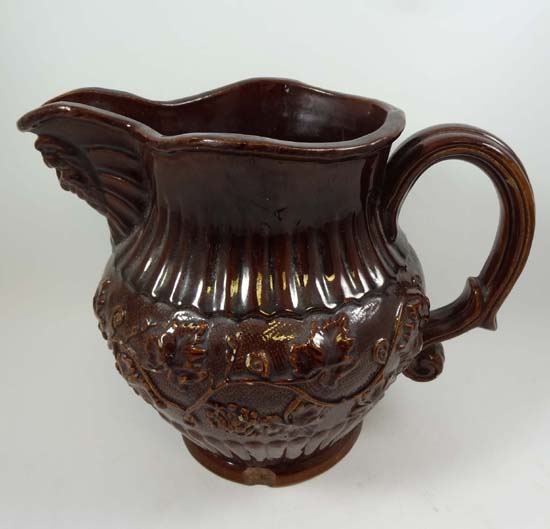 A 19thC treacle glazed moulded jug having Bacchus mask spout, and a wide band of trailing fruiting
