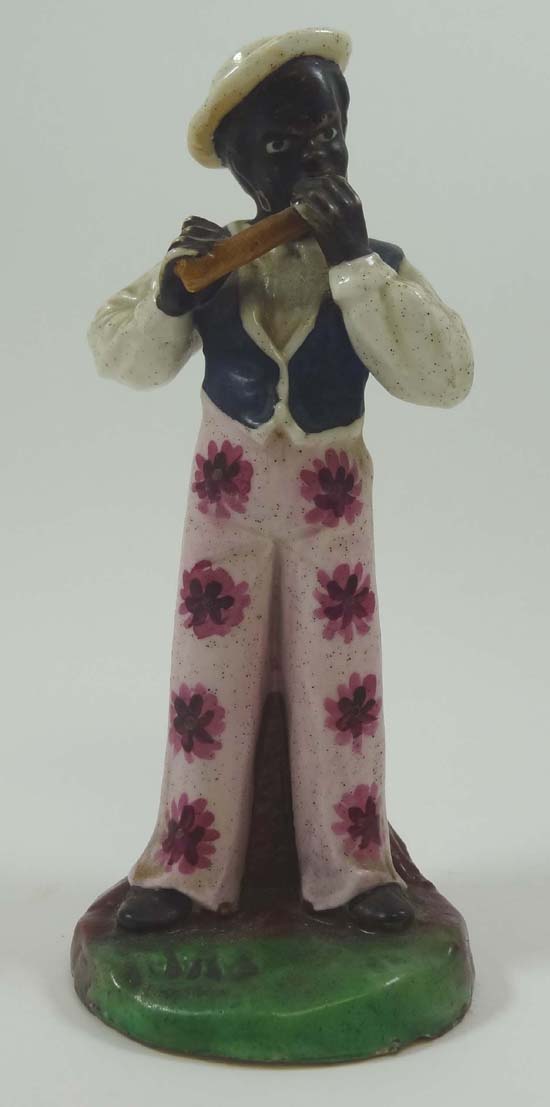 A rare Victorian Staffordshire figure modelled as a black boy playing the harmonica and wearing