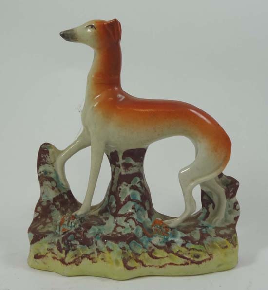 A Victorian Staffordshire figure of a standing greyhound, right front leg raised and standing on a