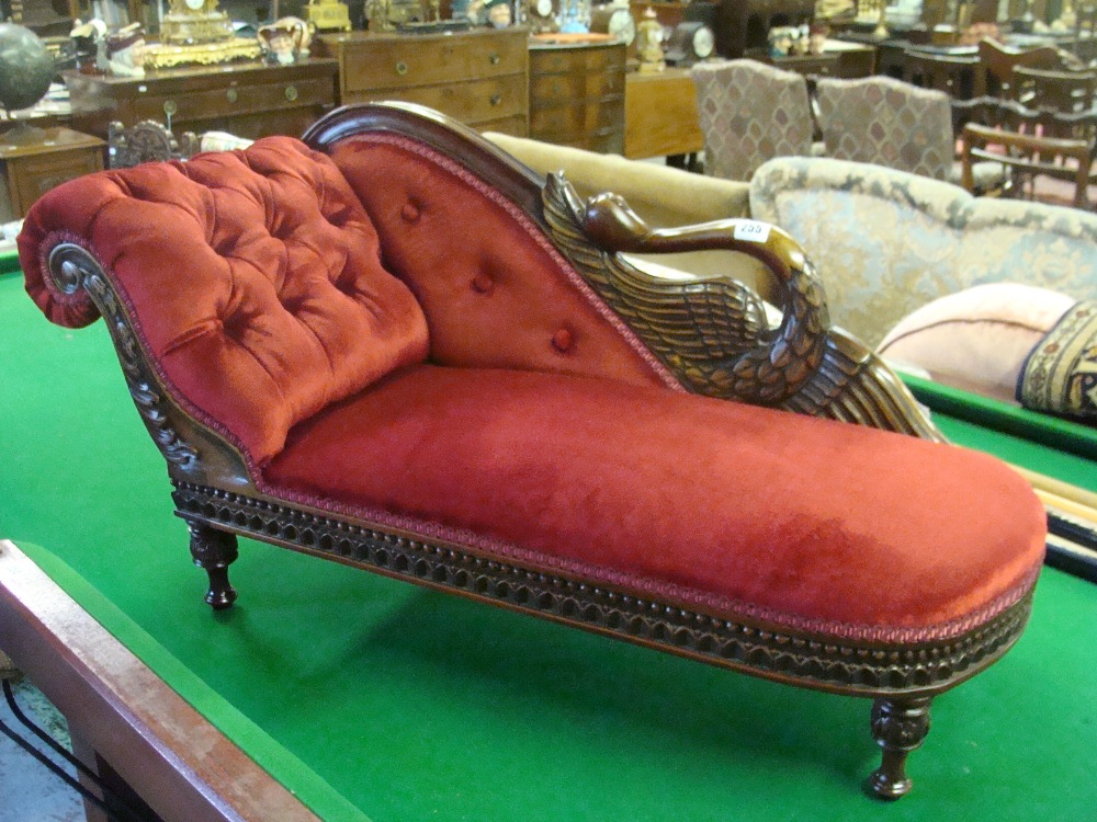 A reproduction carved mahogany framed child`s chaise longue upholstered in red material