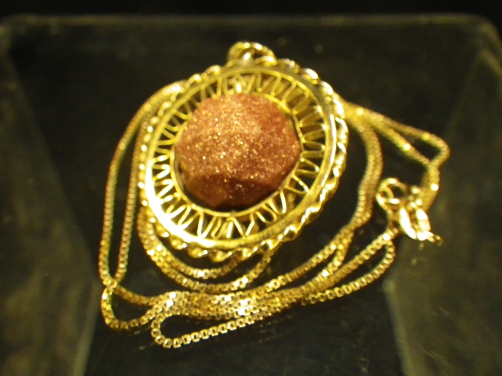 A faceted sand stone bead, set in gold as a pendant on an 18ct yellow gold box link chain