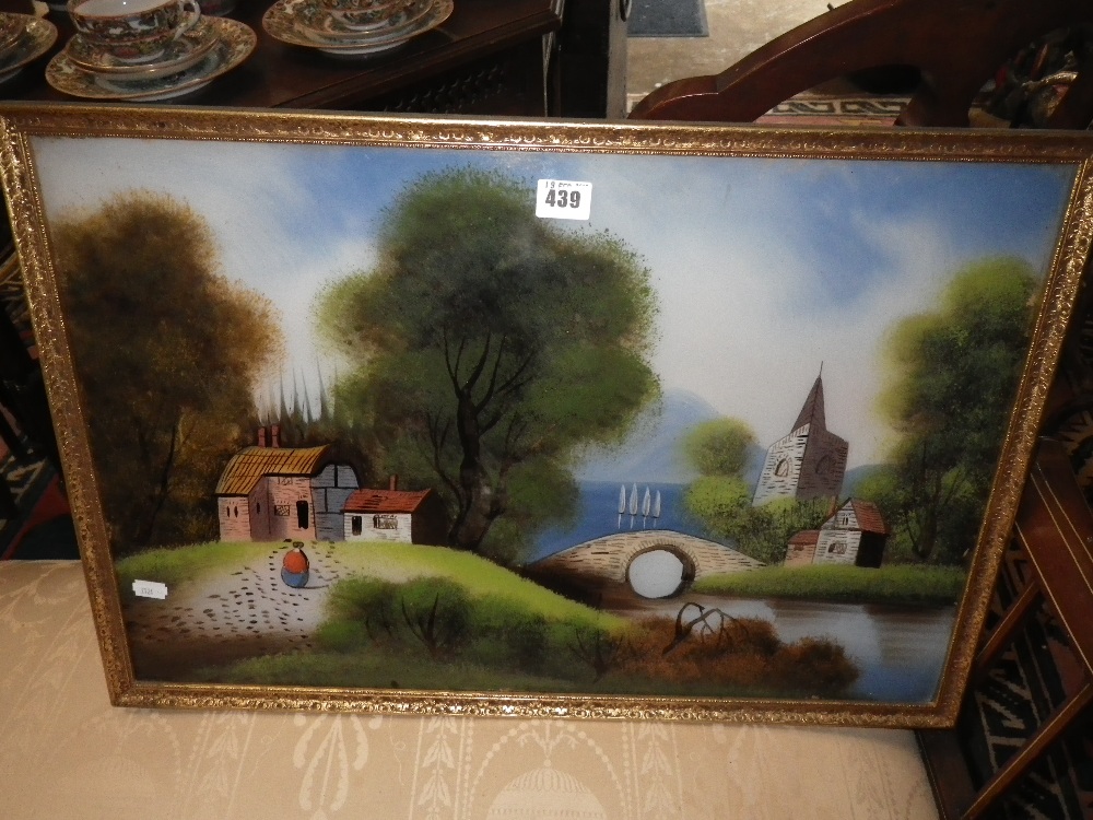 A Victorian reverse painted glass picture depicting cottages, a bridge and a church