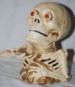 A vintage style cast metal halloween money box in the form of a skeleton. When operated, the coin