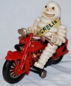 A vintage style Michelin Man bibendum figure, made of metal, depicted riding a motorcycle.