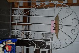 A wrought metal garden gate painted white in recoco form along with vintage lawn mower and grass