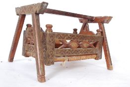 An Indian wooden and brass worked childs swing crib / cot having rope woven bed with intricately