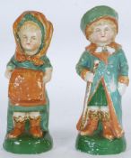A pair of continental china figurines of a boy and girl in green attire. 21cm tall.