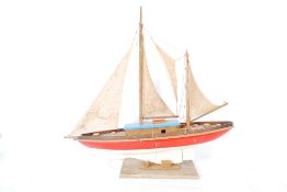 A 1940`s model pond yacht having a wooden construction and canvase sails being raised on a later
