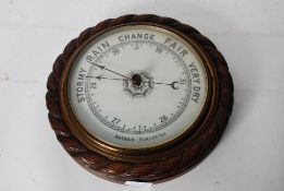 A vintage wall hanging Aneroid Barometer with carved surround and enamel dial. 28cm diameter.